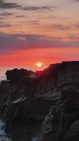 dramatic sunset casting warm colors over rugged coastal cliffs, with ocean waves below and a colorful sky above