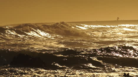 des vagues violentes s'écrasent sur le rivage rocheux lors d'un coucher de soleil doré - prise de vue statique large