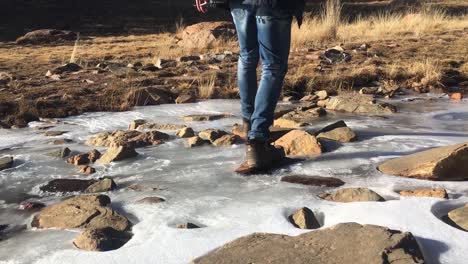 hombre con botas pisando rocas en el río congelado