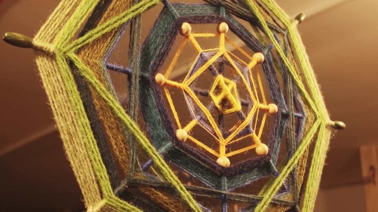 Handcrafted string decoration displayed indoors, vibrant threads, polygon shapes