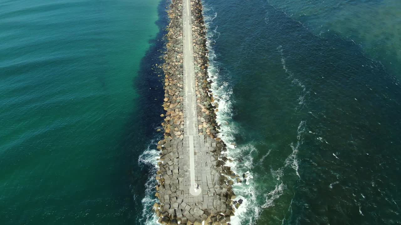 vista aérea desde el final de la vía marítima de la costa dorada que sube hacia la playa, destacando el verde profundo del mar mientras se funde con el azul