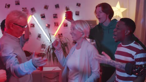positive senior couple dancing with young people at house party