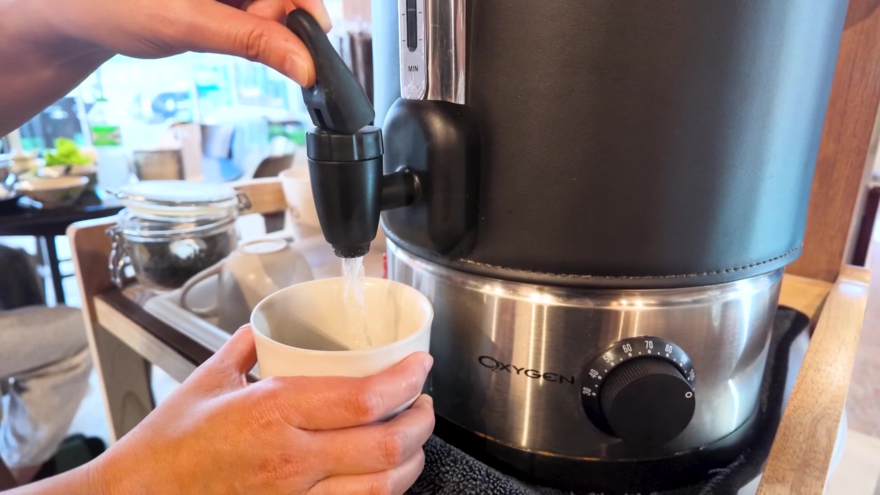 バンコクで電気給湯器から湯気の立つ熱湯をマグカップに注ぐ手