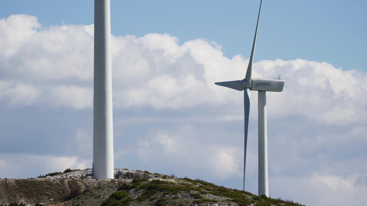 Wind turbines stand tall on a green hillside, with white clouds drifting in the background. Great for environmental projects or renewable energy topics.