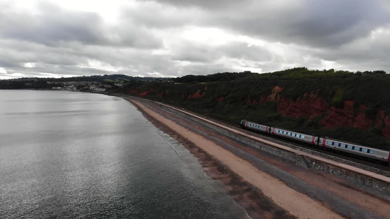 Aerial view of a train travelling along the scenic Dawlish coastline, a popular seaside resort town in Devon, England, under a cloudy sky