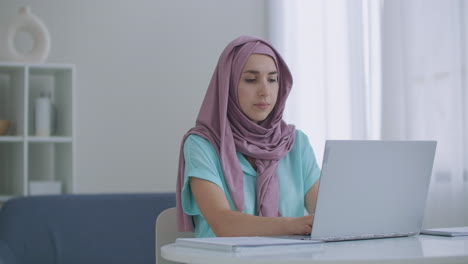 mulher muçulmana trabalhando em um laptop no escritório com seus colegas cristãos. retrato em close-up de jovem empresária muçulmana em hijab usando o laptop dentro do apartamento