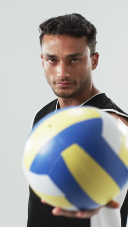 vertical video: biracial male athlete holding volleyball, white background