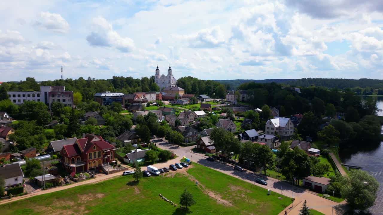 Bright aerial shot of a small Lithuanian town with traditional houses and a baroque church surrounded by trees. Shot in Zarasai, Lithuania