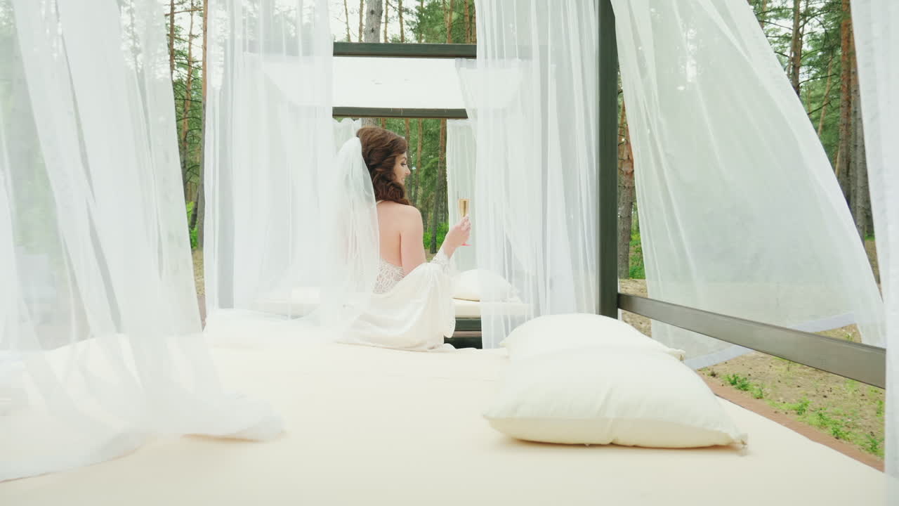 샴페인 한 잔을 든 신부는 수영장 hd 비디오 옆에 있는 안락의자에 앉아 있습니다.