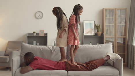 girls stepping on father lying on couch