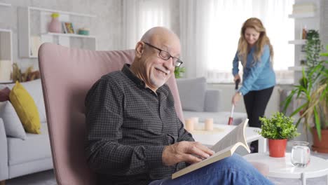 La-Pareja-De-Ancianos-Está-En-Casa-Y-El-Hombre-Lee-Un-Libro-Y-La-Mujer-Limpia.