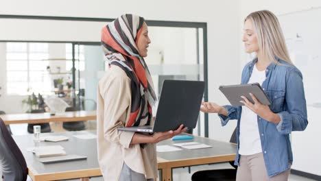 busy diverse businesswomen discussing work with laptop and tablet in office in slow motion