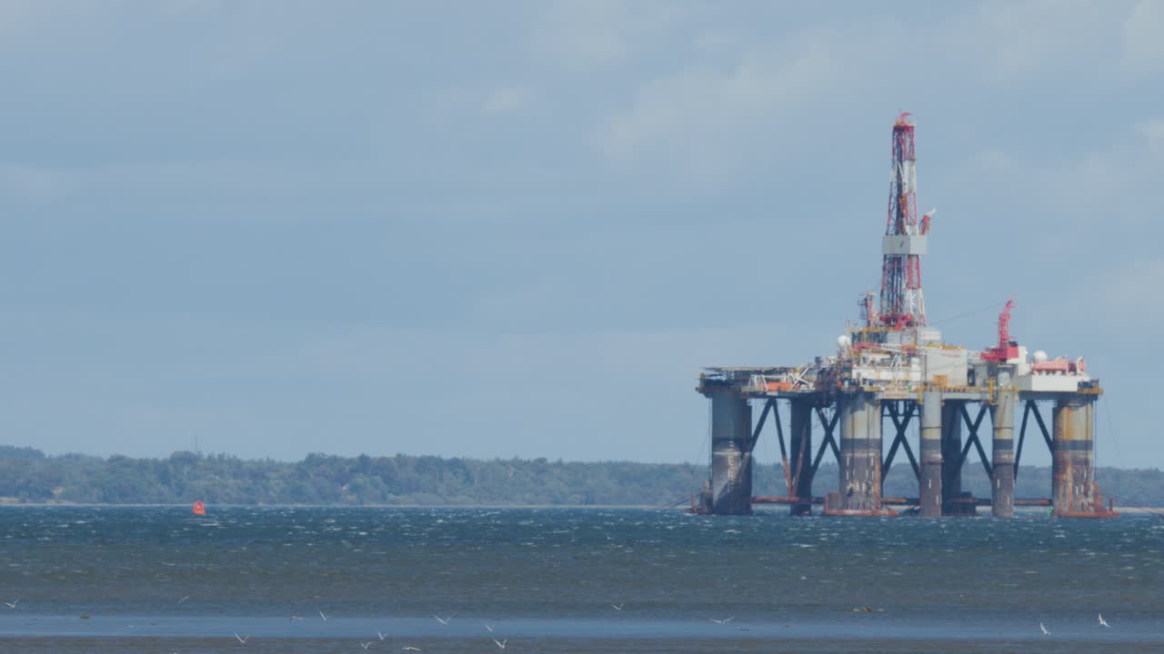 Stationary offshore oil platform in rough sea, viewed from shore under cloudy daylight sky
