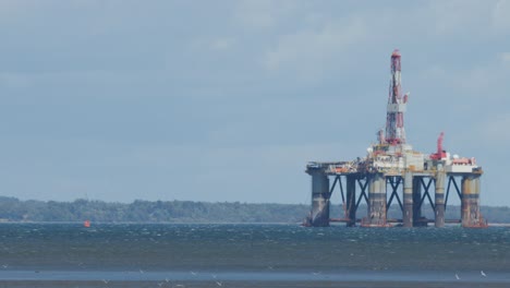 Stationary offshore oil platform in rough sea, viewed from shore under cloudy daylight sky