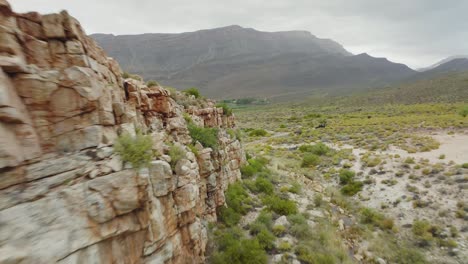 drone flies close to a rock face towards a road where a black off-road vehicle is driving in cederberg wilderness area in south africa - mountains can be seen in the background