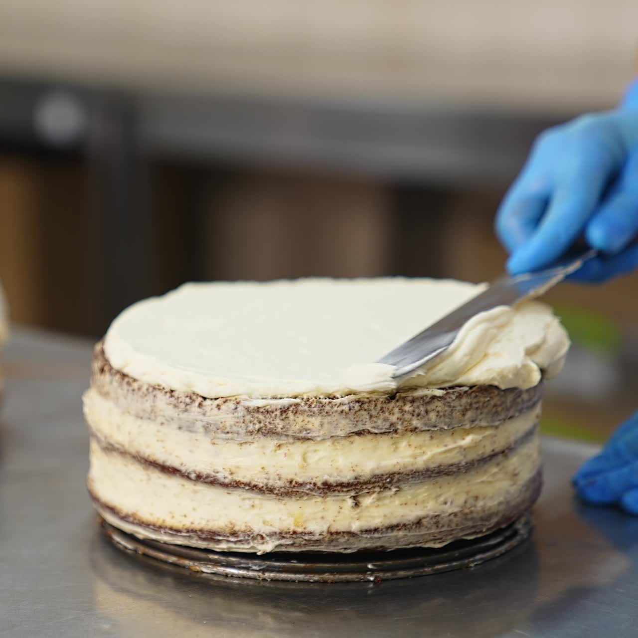 Confectioner spreads thick whipped cream over the top of the cake with spatula. Sweet desserts production at the food factory. Close up
