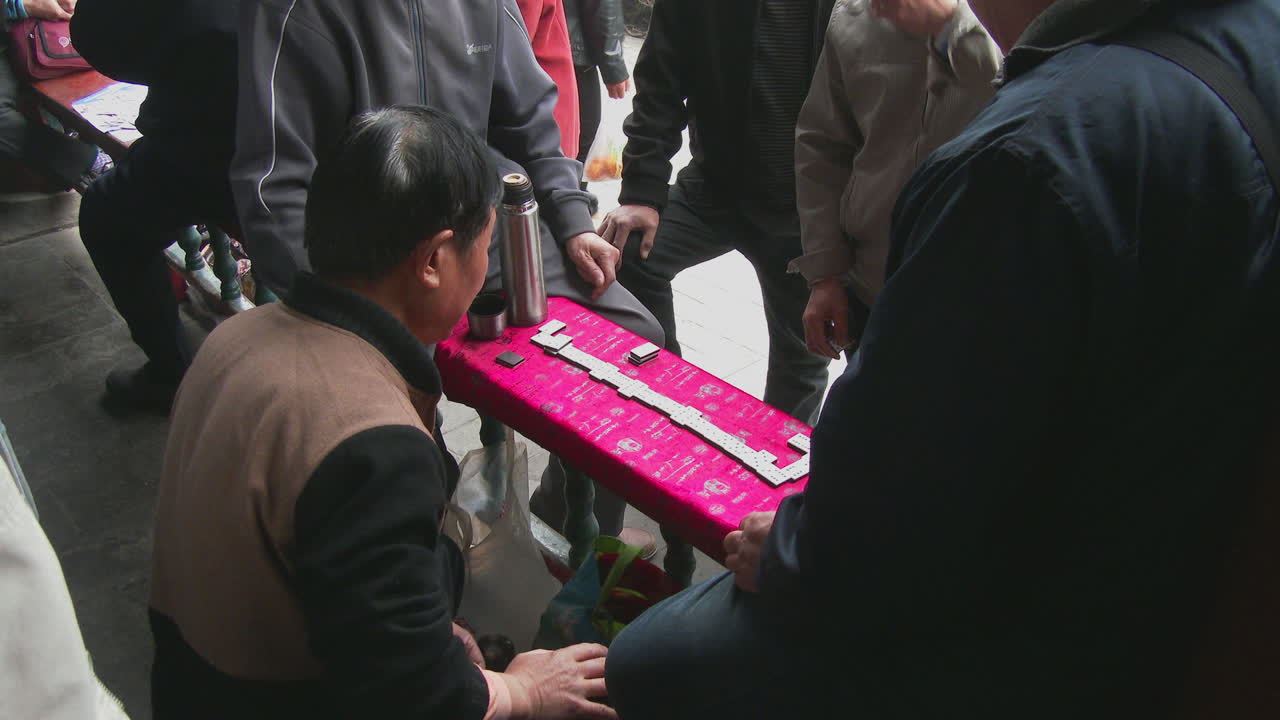 지나가는 사람들이 지켜보는 가운데 중국의 한 공원에서 노인들이 마작을 하고 있다