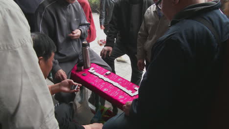 Old-folks-play-mah-jong-in-a-park-in-China-as-passersby-watch