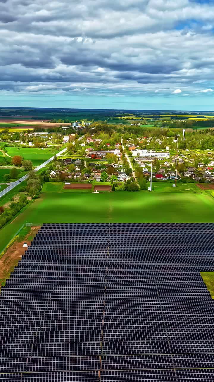 Vertical drone view of thick white clouds passing over city surrounded in greenery. Solar farm in foreground.