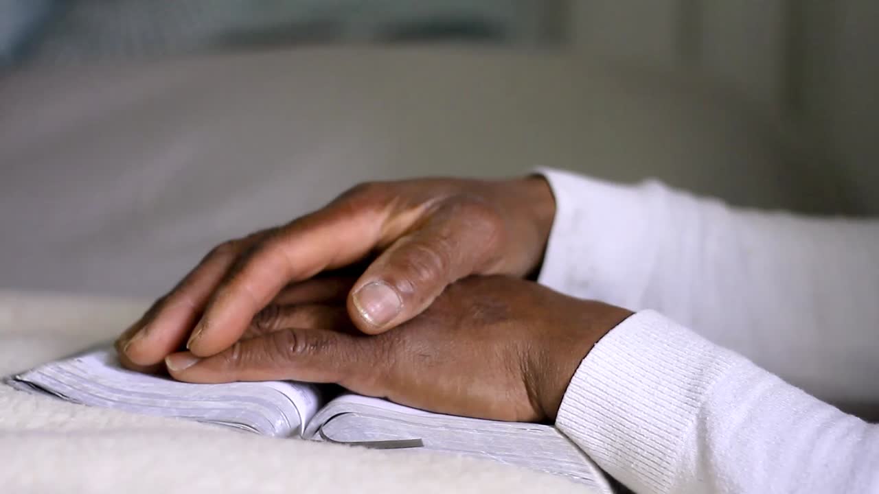 man praying to god with hands together with bible Caribbean man praying with white background stock footage
