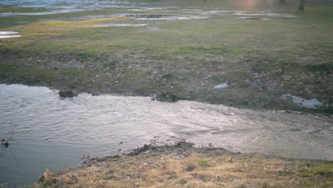 pan of water flowing into sewage system under road by grass field