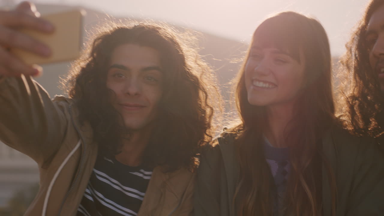 happy group of friends enjoying weekend rooftop party at sunset taking selfie photos using smartphone sharing weekend gathering on social media