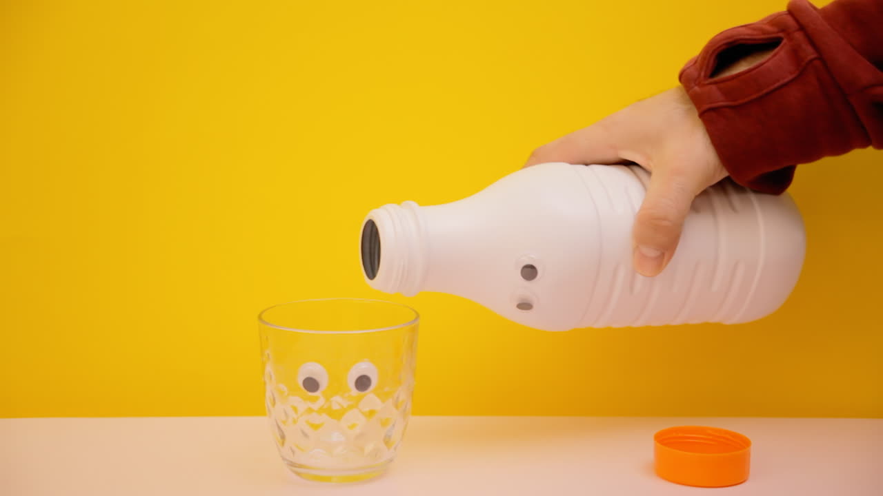 vertiendo leche de una botella de plástico blanca con ojos googly en un vaso con la misma cara graciosa
