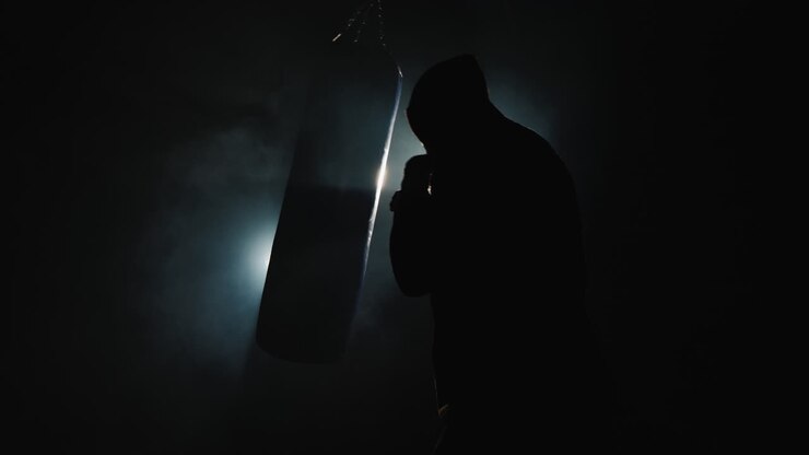 Silhouette di un combattente Trinity in palestra - colpisce un sacco da boxe.