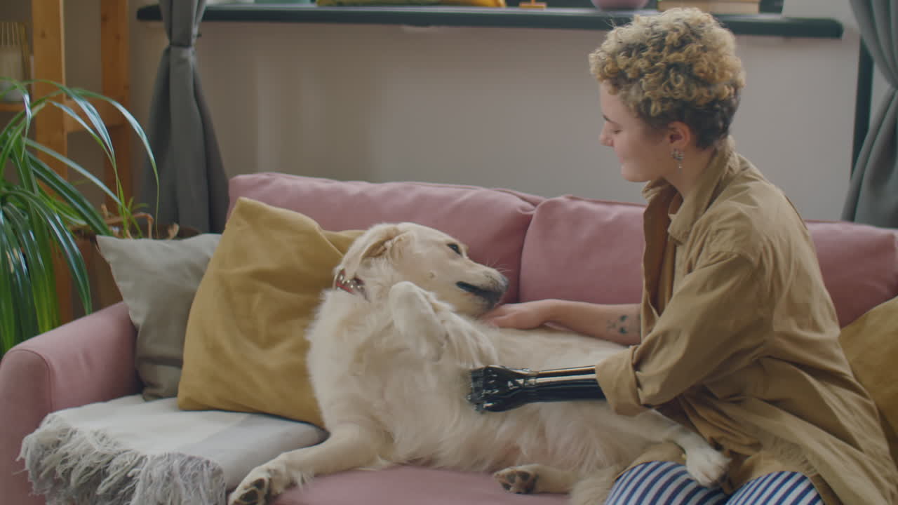 Girl with Prosthetic Arm Petting Golden Retriever Dog on Sofa