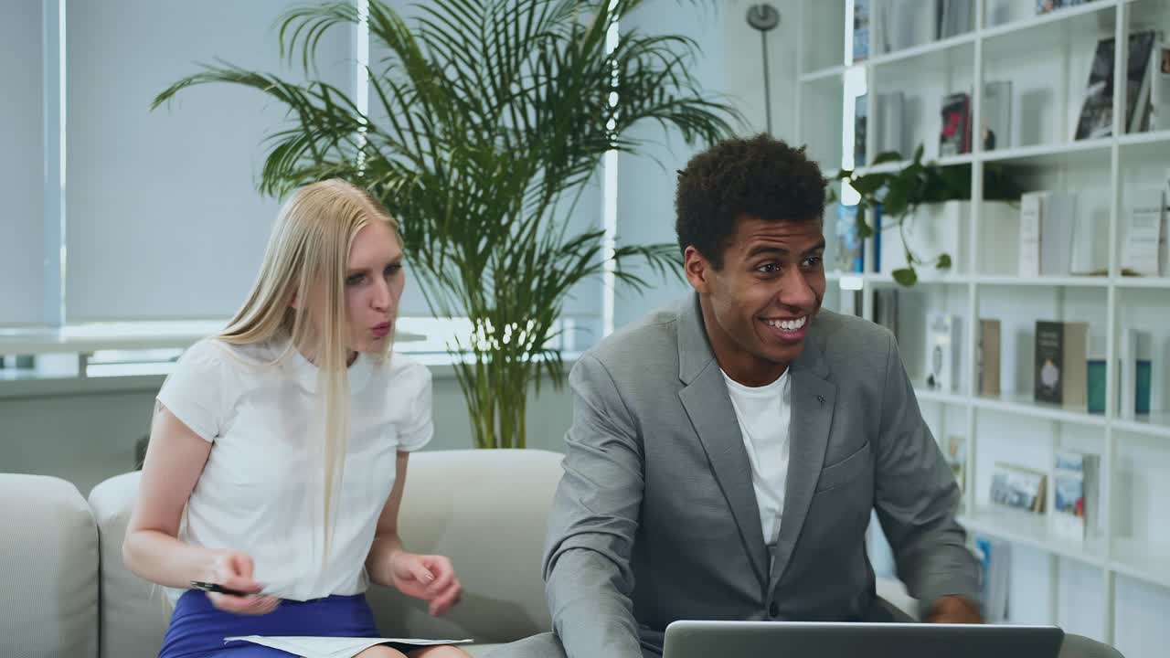 Black man sharing good news with coworkers. African-American man surfing laptop and sharing great news with coworkers sitting together in office around table