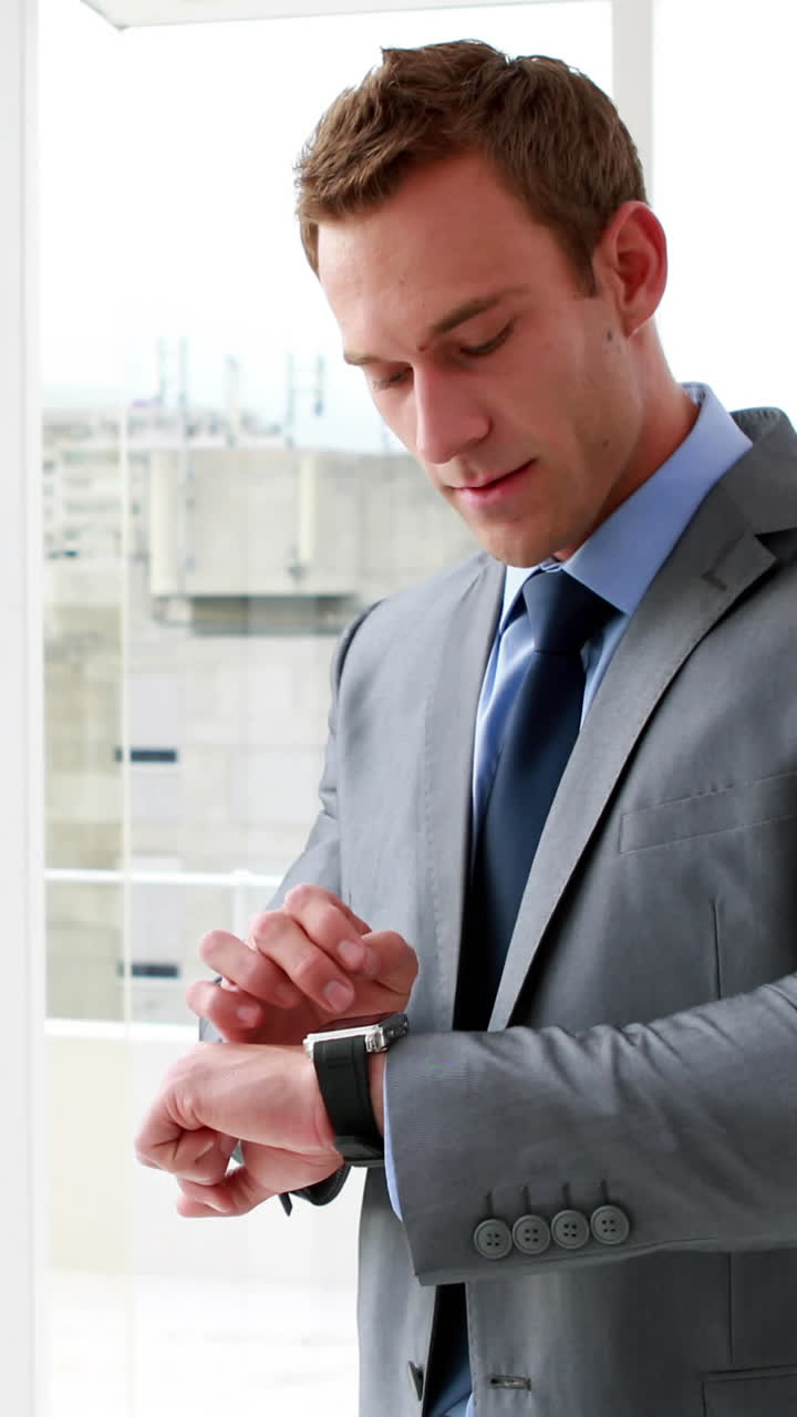 Vertical video of a young Caucasian businessman checks his watch in an office, with copy space