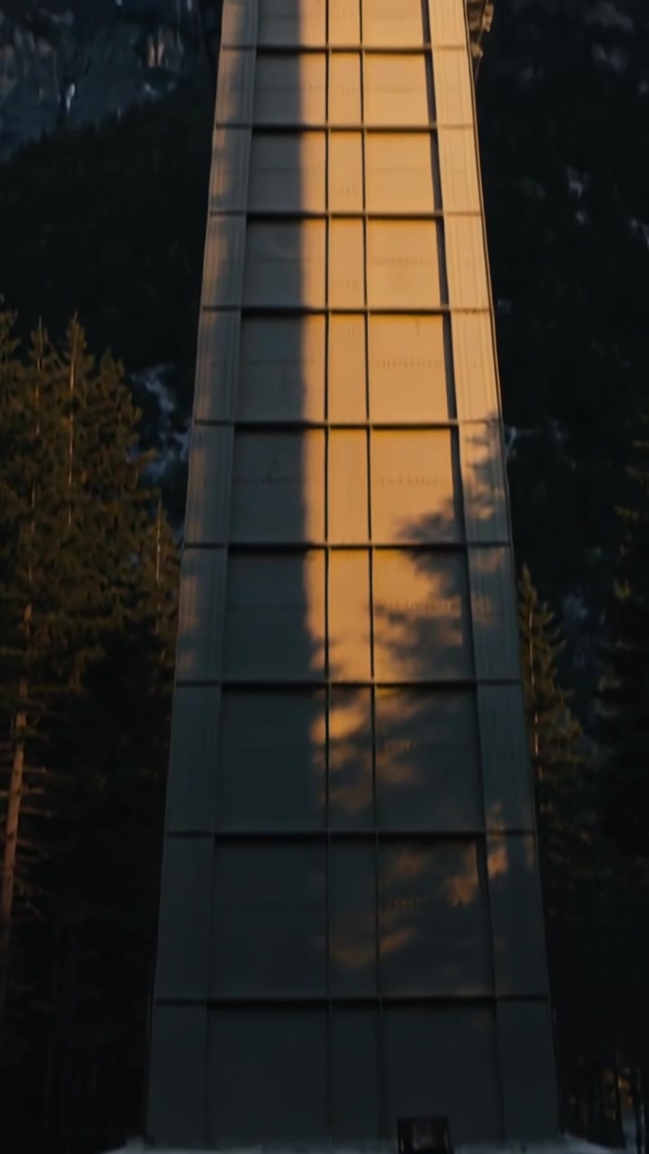 Vertical video: Tilting camera revealing tall metal pylon at clearing, exposing platform and peaks
