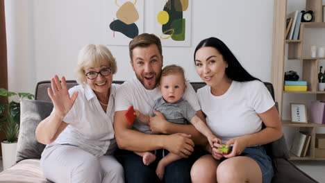 familia feliz sentada en un sofá en la sala de estar saludando y hablando por videollamada 1