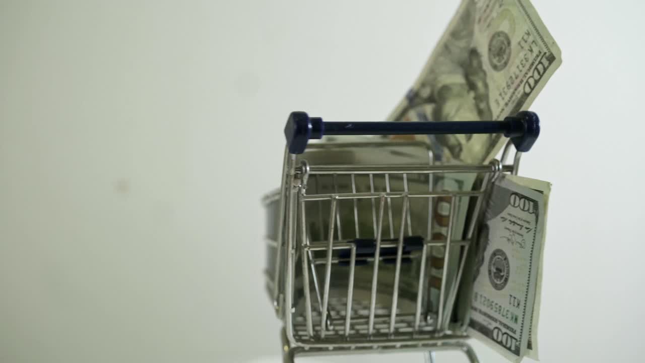 carrito de compras cargado con billetes de 100 dólares girando sobre un fondo blanco