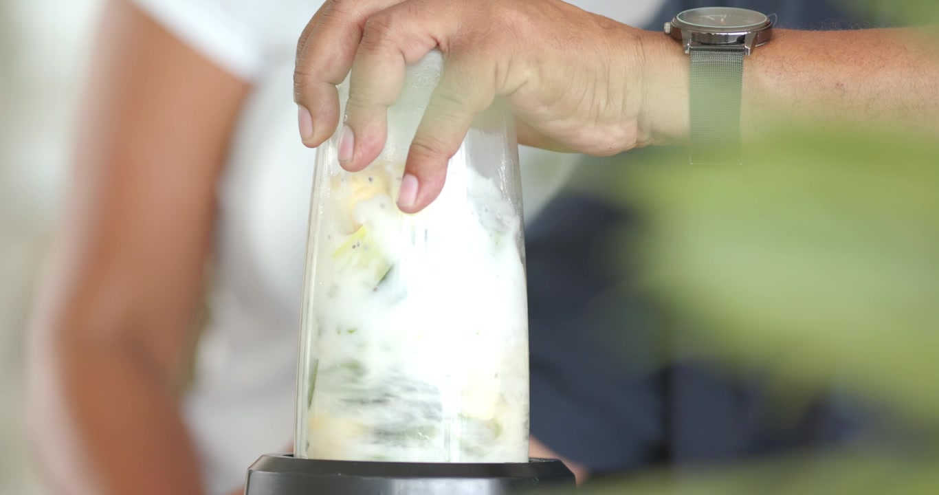 Pasangan Afrika-Amerika di meja dapur rumah, tangan pria menekan wadah pada blender, memblender smoothie.