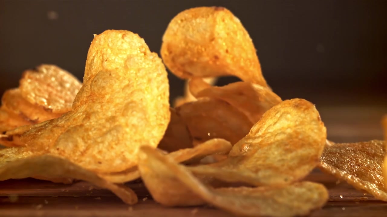 Crispy Potato Chips Falling onto a Wooden Surface in Slow Motion