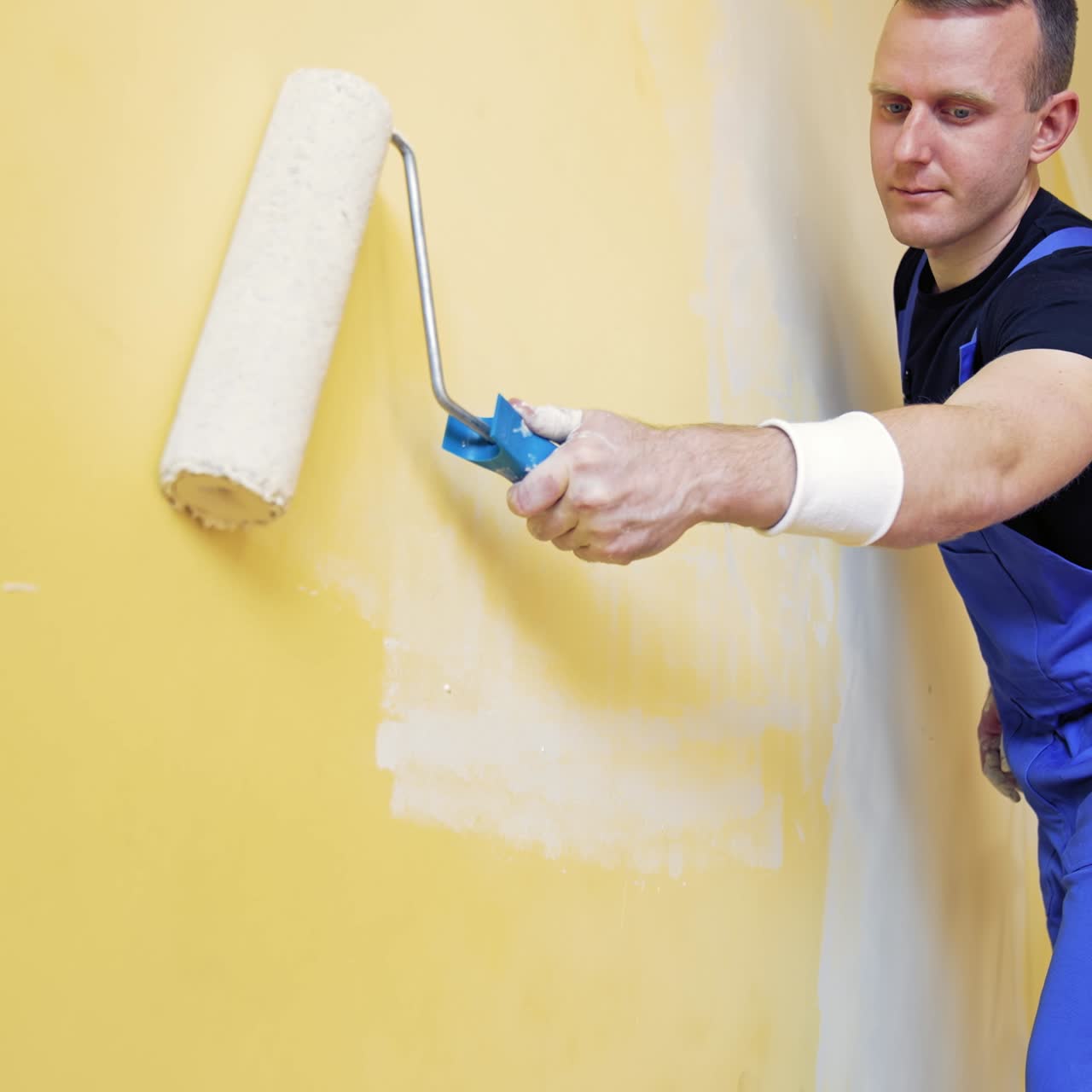 Room makeover. Portrait of a young man who painting wall. Worker painting wall in new color with a paint roller from a ladder indoors