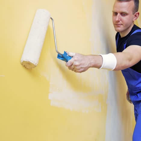 room makeover. portrait of a young man who painting wall. worker painting wall in new color with a paint roller from a ladder indoors