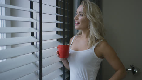 Cheerful-woman-with-mug-looking-out-window