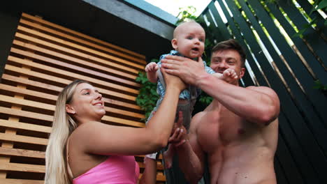 little infant wants to cry as parents hold him. mom and dad start to wave a baby and he smiles. low angle view.