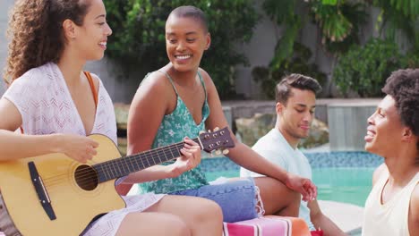 mujer biracial feliz tocando la guitarra y cantando con un grupo de amigos diversos en una fiesta en la piscina