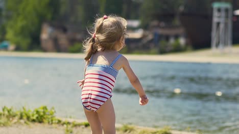 close-up slow motion little girl in bathing suit throws stone at lake on beach