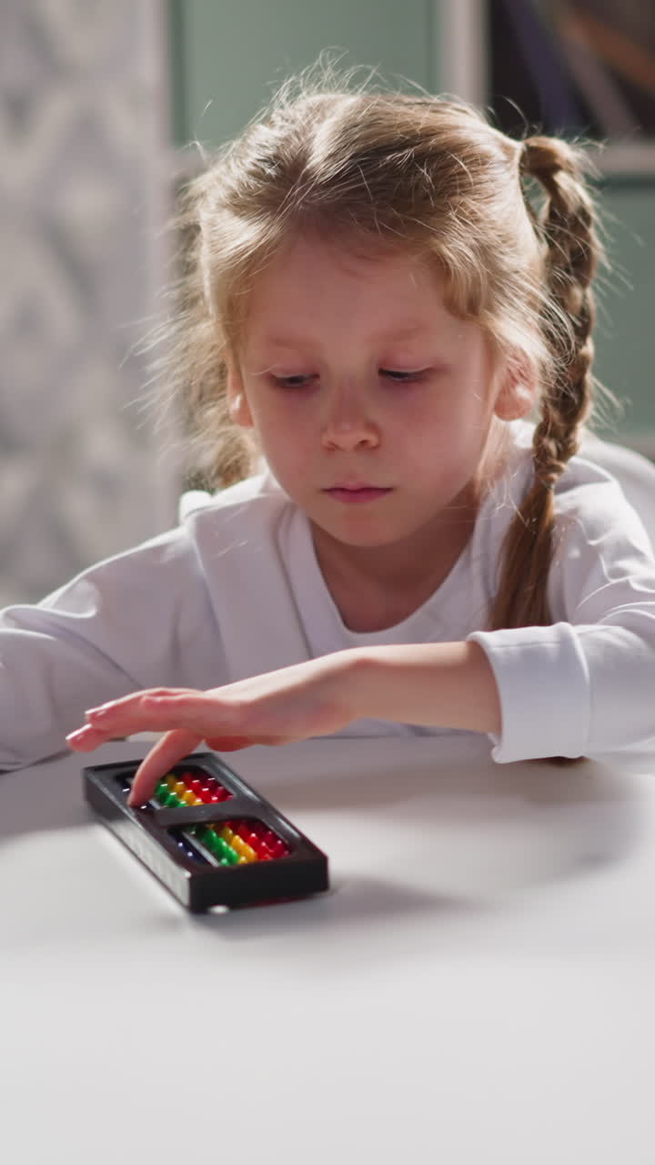 Bored little girl preschooler with plaits turns colorful abacus entertaining at workplace during mental mathematics lesson closeup slow motion