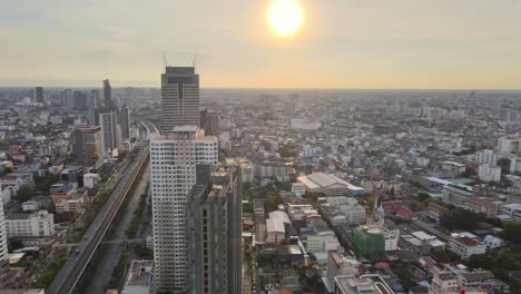 Man-standing-on-top-of-a-roof,-drone-fly-over,-while-camera-in-hand-at-Sunset