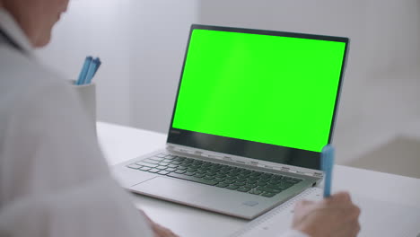 una doctora está escuchando una conferencia en línea en videoconferencia en una computadora portátil pantalla verde en una computadora portátil para la tecnología de clave de croma vista detallada