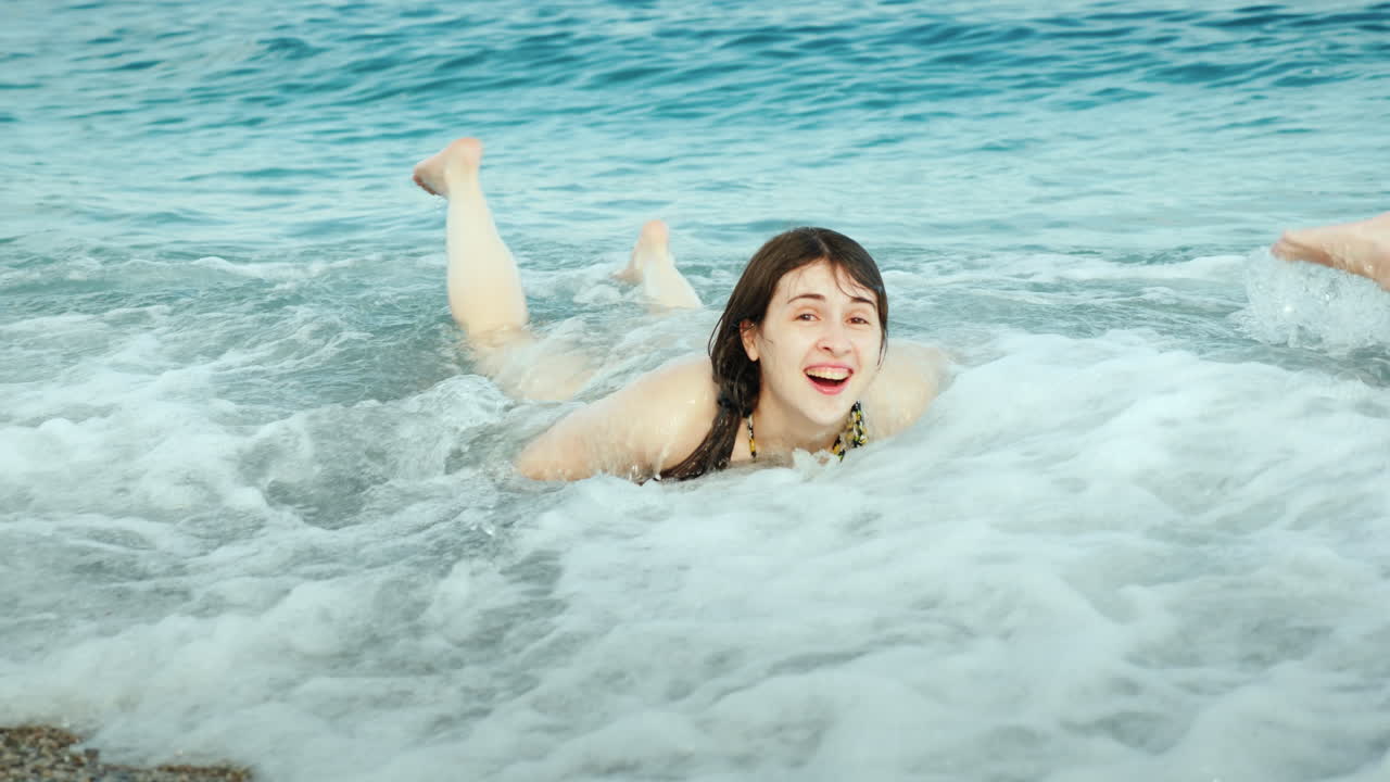 활발한 휴가 비키니를 입은 예쁜 소녀가 해변에서 즐거운 시간을 보내고 있습니다. 큰 파도가 튀고 있습니다.