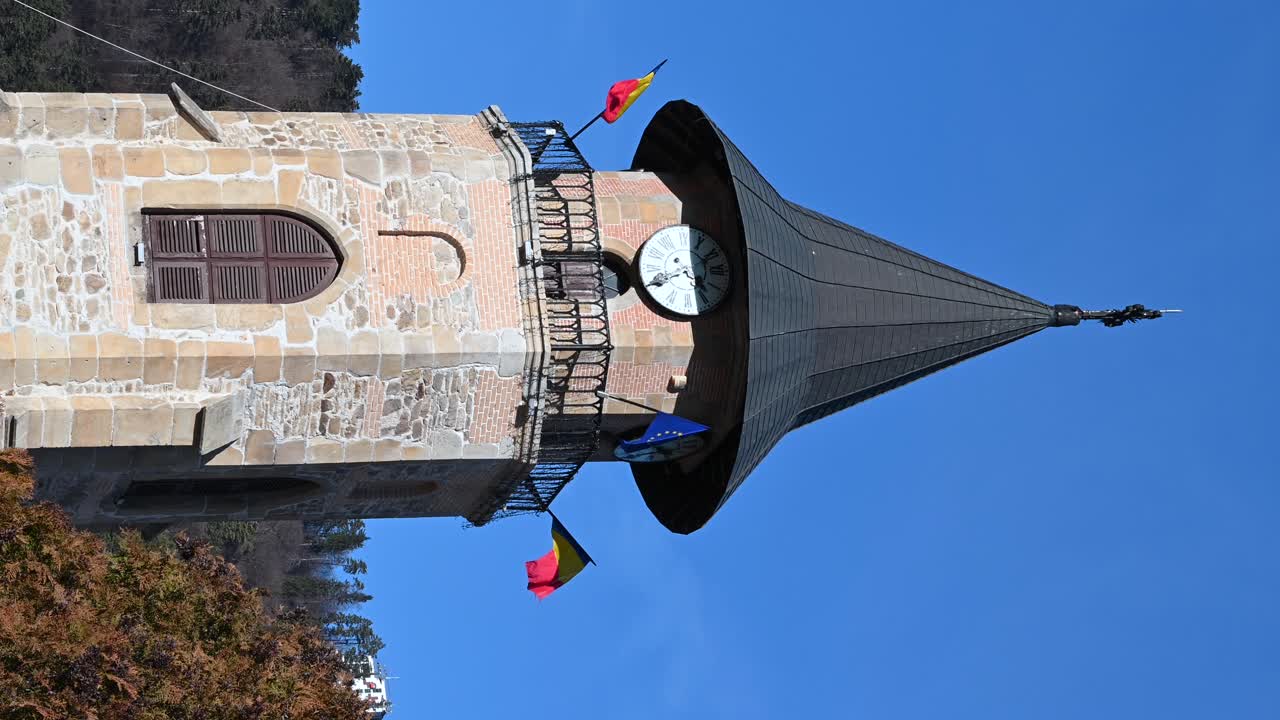 Close up of a Tower bell with the Romanian and European Union flags in Piatra Neamt, Romania on a blue sky background. Vertical