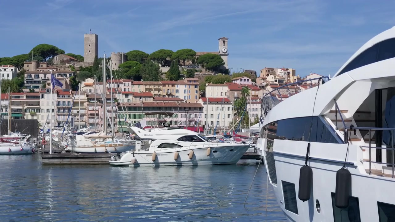 Vista ravvicinata della prua di uno yacht di lusso con un motoscafo e un centro storico collinare sullo sfondo, Cannes, Francia.
