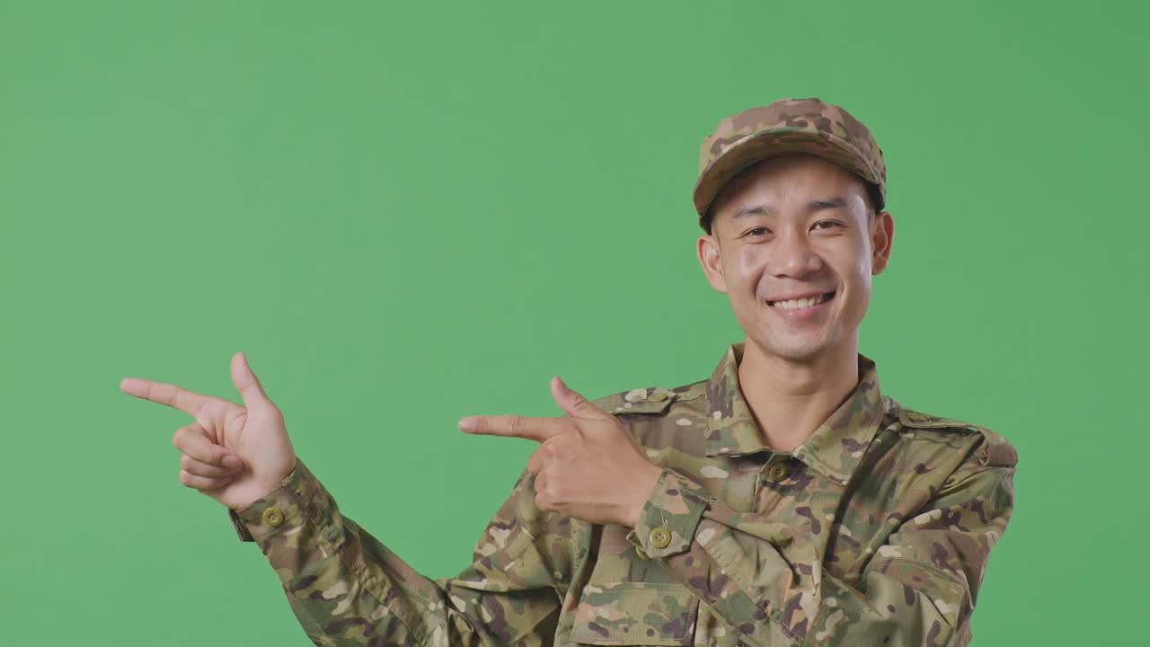 Close Up Of Asian Man Soldier Smiling And Pointing To Side While Standing In The Green Screen Background Studio