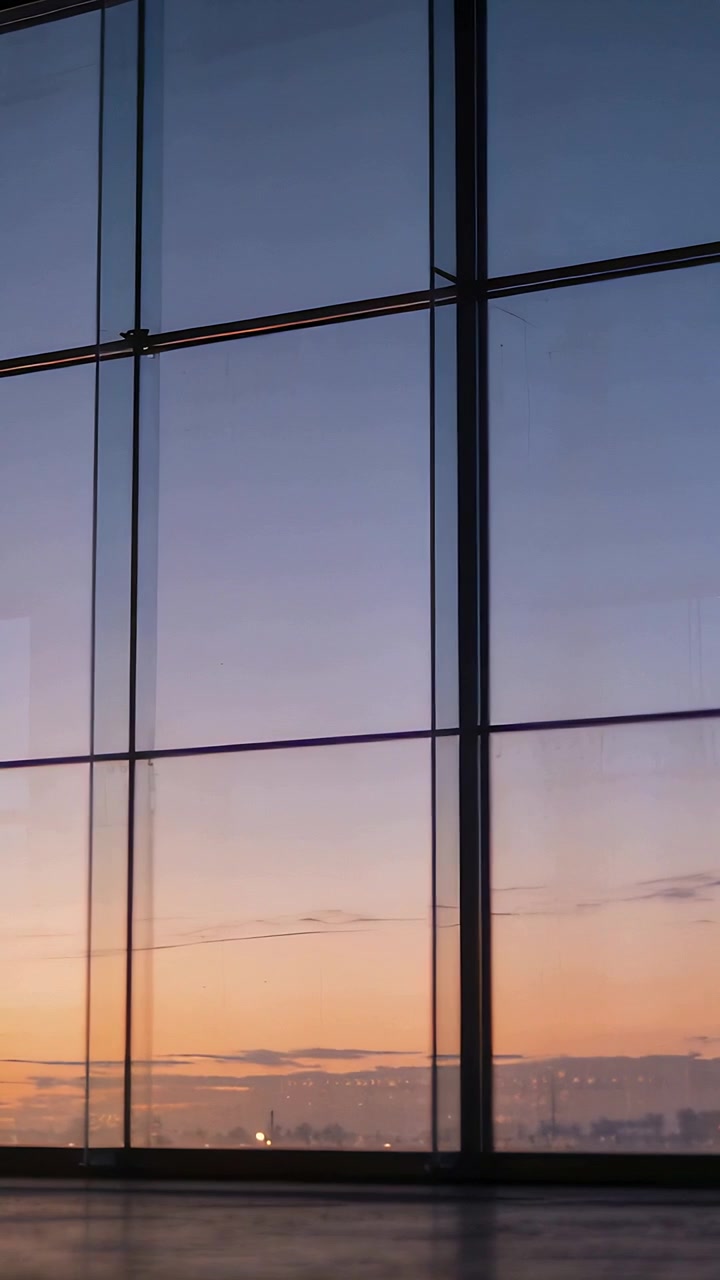 Video verticale: Inquadratura di una parete di vetro a tutta altezza con la telecamera che panoramica nella hall, mostrando le sfumature dell'alba.
